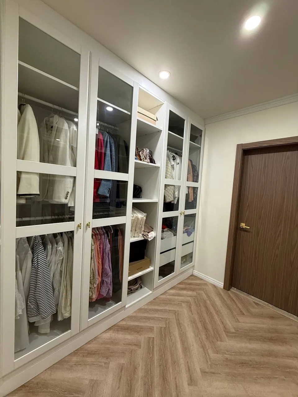 Full-height storage wall with glass doors, shelving, and hanging sections