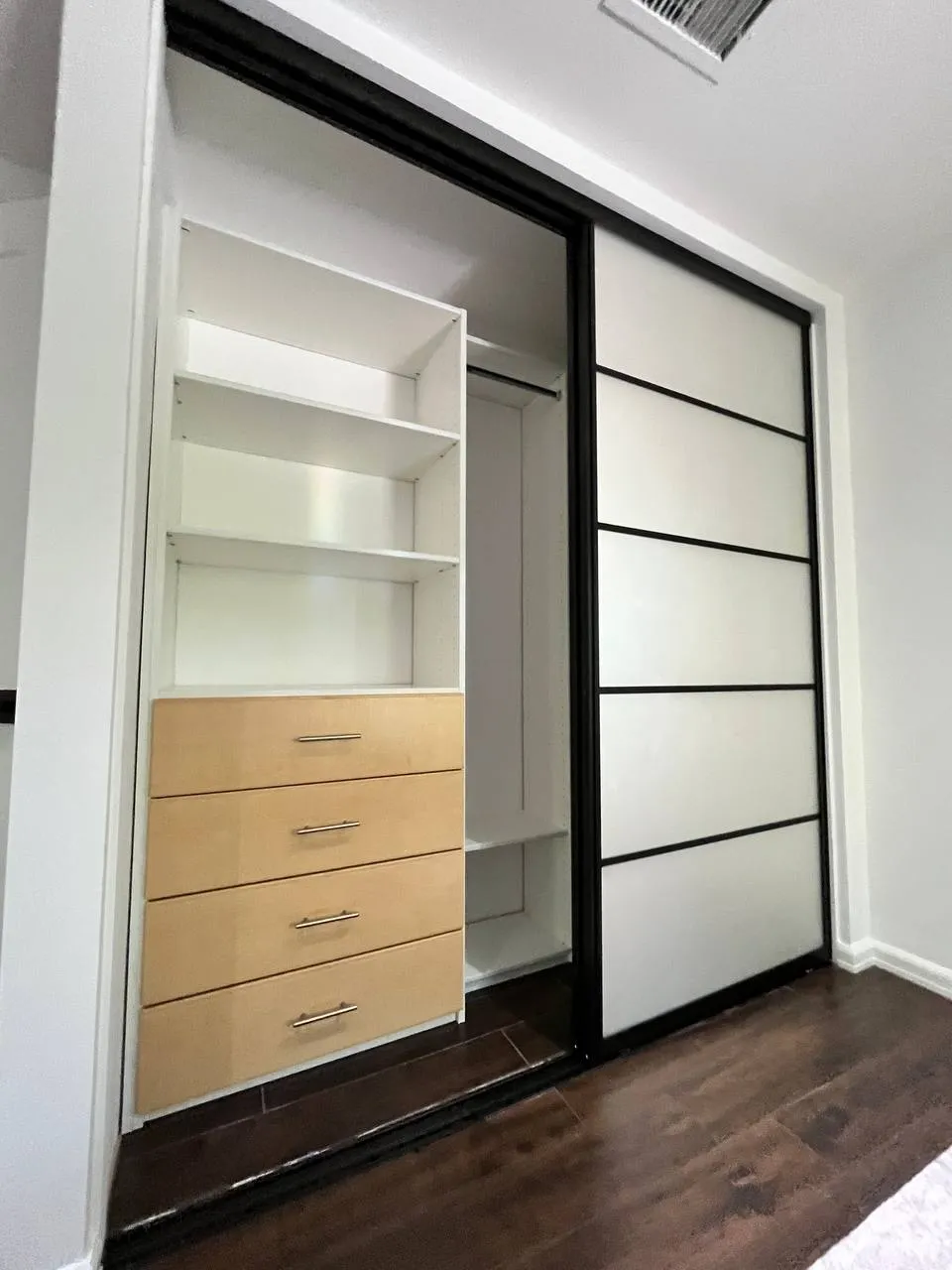 Custom reach-in closet with white shelving, wood-tone drawers, and black aluminum sliding doors in Calabasas