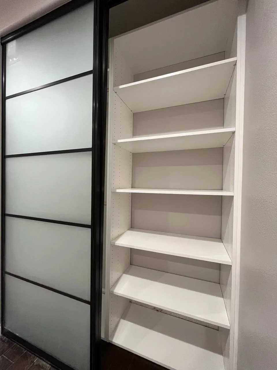 White melamine reach-in closet shelving beside black aluminum frosted glass sliding doors in Moorpark