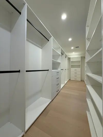 Full walk-in closet layout with white cabinetry, shelves, drawers, and black rods